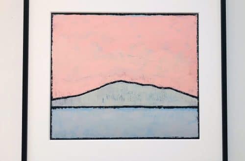Framed abstract landscape painting: pink sky, dark ridge, and pale blue water on a white wall.