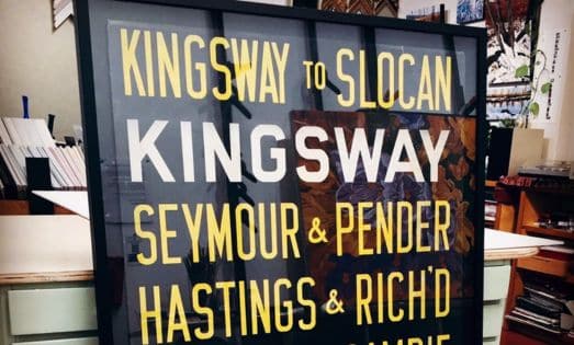 Framed signboard in a store listing street names: KINGSWAY, SLOCAN, SEYMOUR & PENDER, HASTINGS & RICH'D? with bold yellow and white letters.