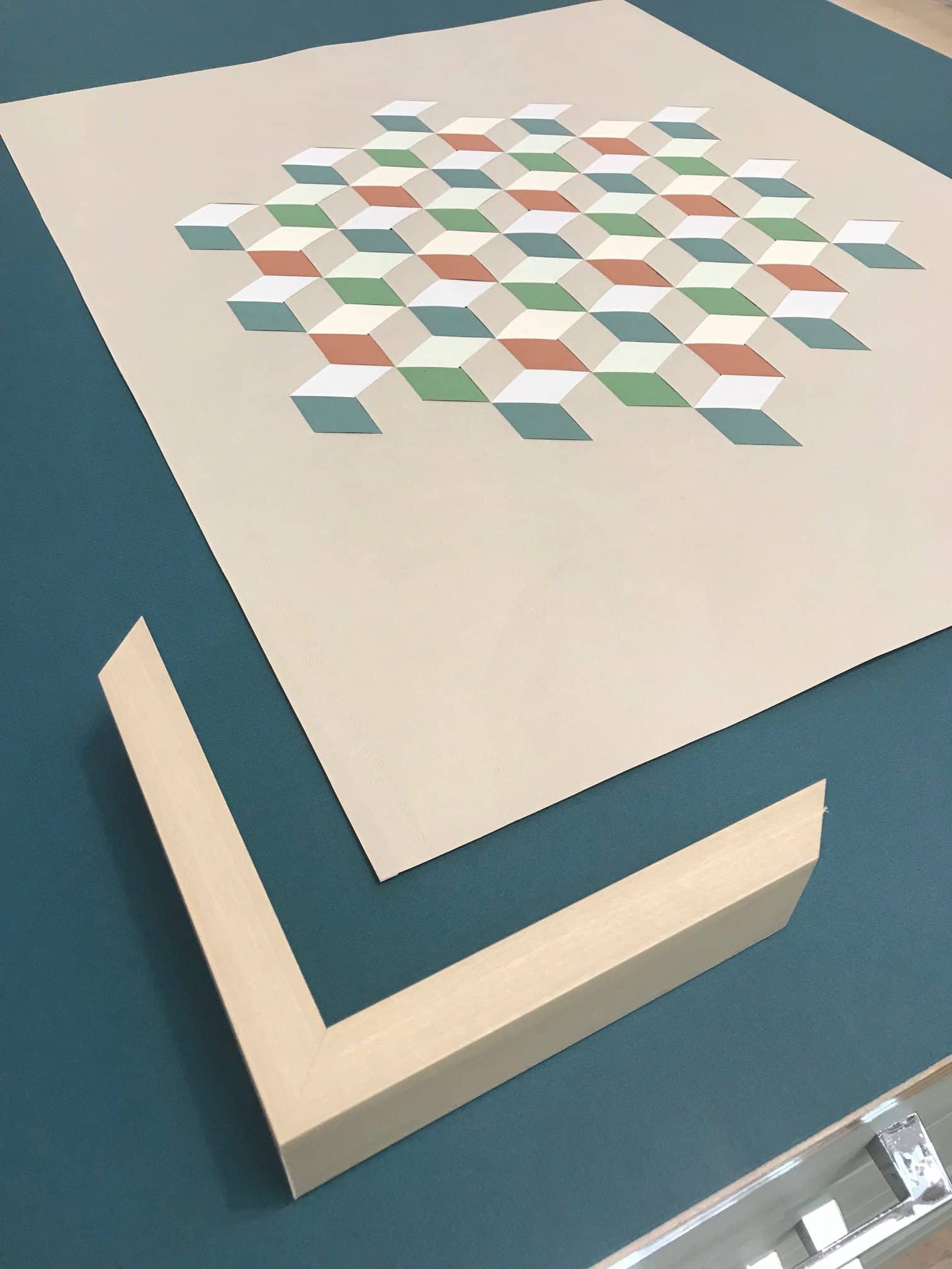 Abstract geometric pattern of small tiled cubes in pastel colors on a pale square board on a blue surface.